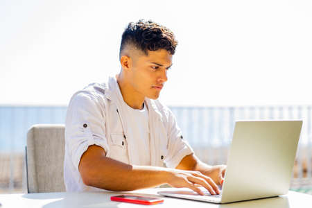 young freelance man in white shirt working by laptop in beach cafeの写真素材