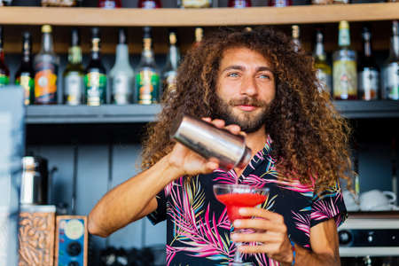 Handsome smiling curly hair bartender preparing cocktail at the resort bar