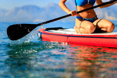Woman sitting on sup board and enjoying peace and quiet outdoors .