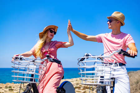 Happy casual couple in pink outfits take for rent a bike ride on the pier on a sunny dayの写真素材