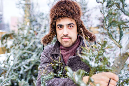indian man in stylish wool coat buys a Christmas tree outdoors snow backgroundの写真素材