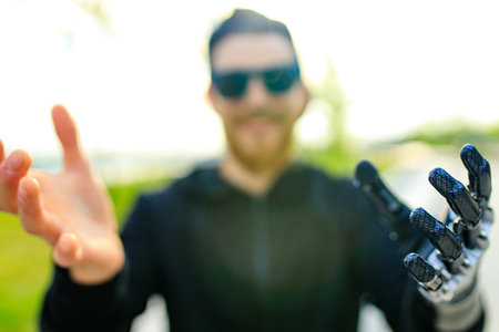 young bearded man with metal arm prosthetic outdoorの写真素材