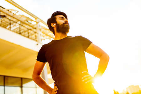 latin hispanic man in black cotton t-shirt witn an earpons warming up outdoor at sunset golden lightsの写真素材