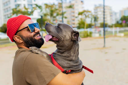 portrait of happy man in red hat and sunglasses with american terrier in dogs walking area park in sityの写真素材