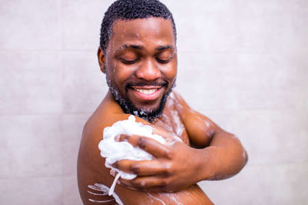 brazilian man washing body with shower sponge in white bathroomの写真素材