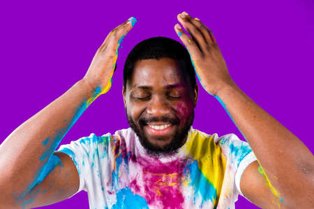 latin brazilian male in white cotton t-shirt with colorful paint of face laughing studioの写真素材