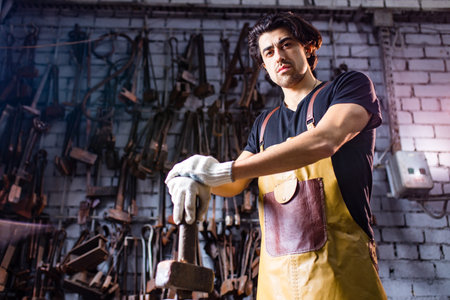 Authentic blacksmith man forges a metal product in dark indoors studio