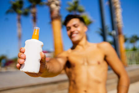 Strong brazilian man with a helathy body using spf cream in sunny day at beachの写真素材