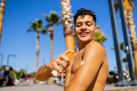 latin man applying suntan lotion at sea with palms background