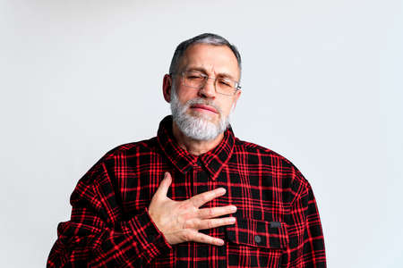 Portrait of mature man isolated on grey background suffering from severe heart ache, closing eyes to relieve painの写真素材