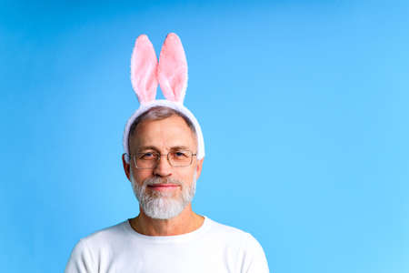 Cute mature man with bunny ears ready to Easter festivale on blue color backgroundの写真素材