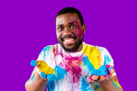 Afro american man celebrate holi festival in violet studio backgroundの写真素材