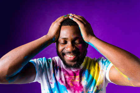 latin brazilian male in white cotton t-shirt with colorful paint of face laughing studioの写真素材
