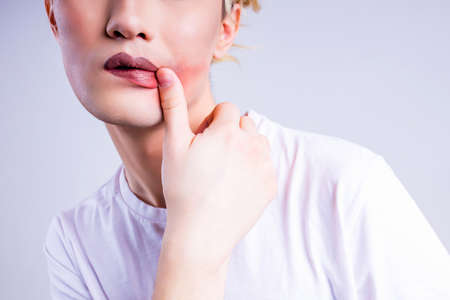 Closeup portrait of a young androgynous man smearing his lipstick ipstick over white backgroundの写真素材