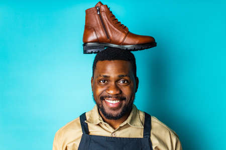 latin hispanic man in black apron showing brown leather shoes in blue studio backgroundの写真素材