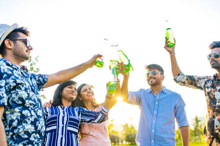 pakistanian happy best friends partying with lemonade and beer in summer parkの写真素材
