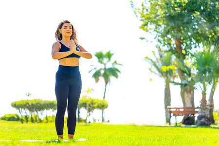 Young indian attractive woman practicing yoga , deep calm breathing outdoors in summer green parkの写真素材