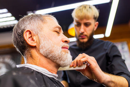 retired man visiting barbershop , sitting in the barbers chair while getting cool hairstyleの写真素材