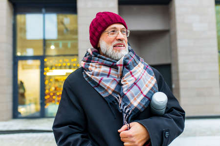 trendy old good-looking man walking in sity street at winter near modern buildingの写真素材