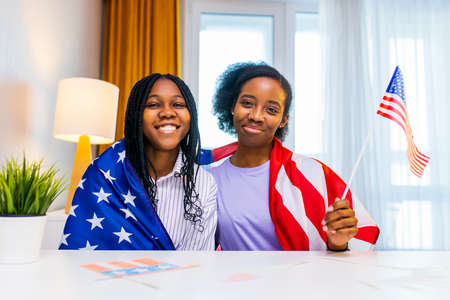 two happy african american sister celebrating usa independence day at home in cozy apartmentの写真素材