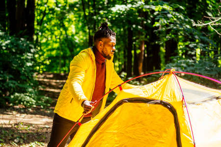 african american in yellow jacker putting on a tent in forestの写真素材
