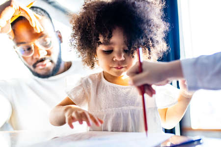father wearing glasses and adorable little daughter drawing colorful pencils spending leisure time on weekend togetherの写真素材