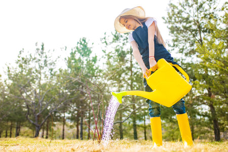 beautiful schoolgirl teenager spending time outdoors in garden wear straw hat and yellow rubber shooesの写真素材