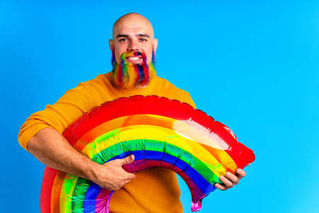 man with colorful beard holding big rainbow balloon in bludio backgroundの写真素材