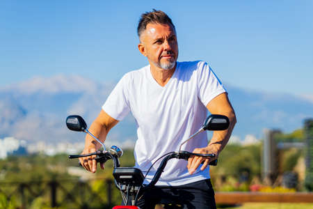 retiree happy man with gray beard have a rest in nature near eco scooter with amazing view on mountains ans beachの写真素材