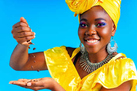 beautiful africa-american woman with yellow turban ower the head showing fresh coffee beand in...