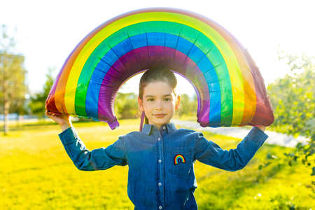 cute little brunette girl holding an air colorful rainbow balloon in summer park