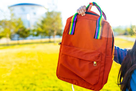 somebody showing an orange rainbow backpack in summer park outdoor