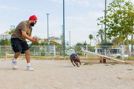 handsom man in red hat and sunglasses training dog outdoors in sity park zone dog walking area...