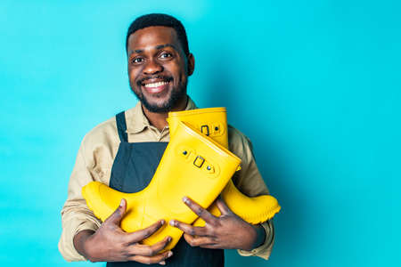nigerian gardener man showing a yellow rubber shoes in blue studio ready for autumn spring seasonの写真素材