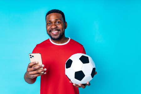 latin hispanic man with phone and football ball in studio blue backgroundの写真素材
