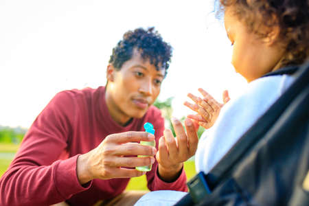 african american father and little girl are useing an ntibacterial gel in summer park outdoorsの写真素材