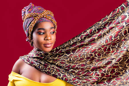 authentic multicultural race boho fashion lady with makeup and silk turban over head in red studio backgroundの写真素材