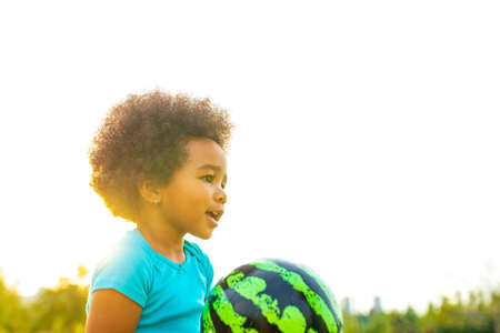 cheerful girl with afro curly hair playing with green ball like a watermelon outdoors