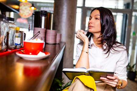 indian reading notes in notepad while sitting near table bar and drinling cup of tea