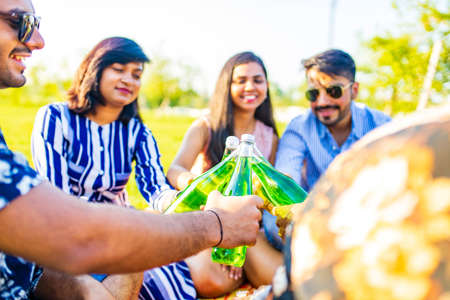 pakistanian happy best friends partying with lemonade and beer in summer parkの写真素材