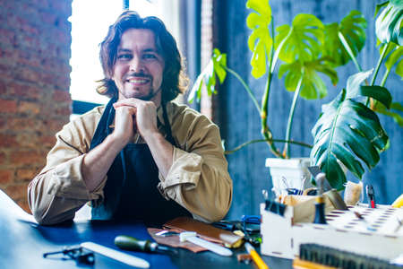 hobby became a small business leather man in apron is making a leather wallet and shooes in studio