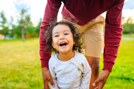 Young pretty dad and his little curly daughter walk together outdoors at sunset light
