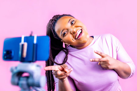 hispanic woman with cool dreadlocks pigtails wear pink dress in studio chatting with her subscribers by phone cameraの写真素材