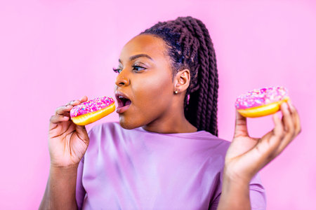 multicultural female holding delicious sweet donut in pink studio backgroundの写真素材