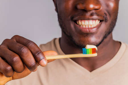 afrian american man holding colorful rainbow toothbrush in gray backgroung