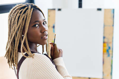 african american woman sitting next to blank white canvas on easel in workspaceの写真素材