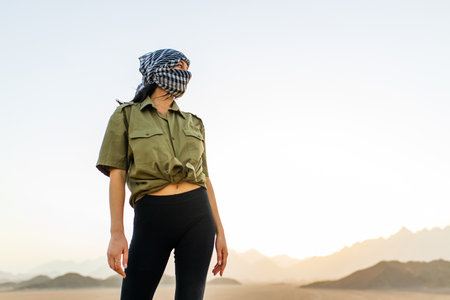 woman with covered head and face with black and white checkered scarf standing desert backgroundの写真素材