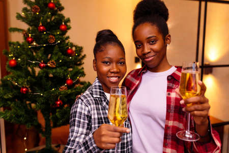 two young latin hispanic couple in love looking at the camera and making a toast congratulations at christmas tree backgroundの写真素材