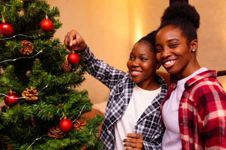 afro married women preparing for New Year winter holidays celebration decorating Christmas treeの写真素材