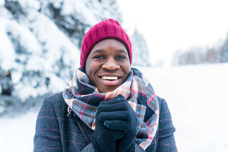 african american handsom man in red hat and stylish plaid coat look at camera with toothy snow-...